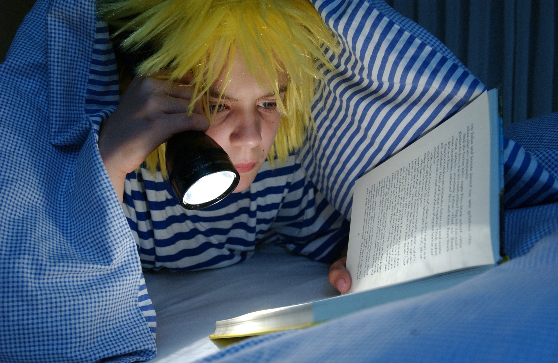 Nuori henkilö lukee kirjaa peiton alla taskulampun valossa