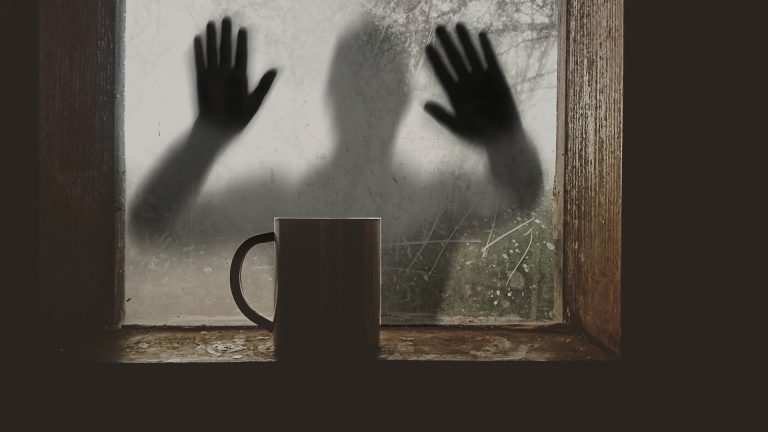 Ihmishahmo ikkunan takana, kämmenet lasissa.